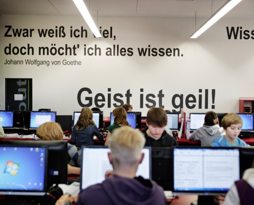 Schülerin und Schüler lernen mit Computern im Lernatelier. Im Hintergrund motivierende Zitate an der Wand: "Geist ist geil!" und "Zwar weiß ich viel, doch möcht' ich alles wissen."